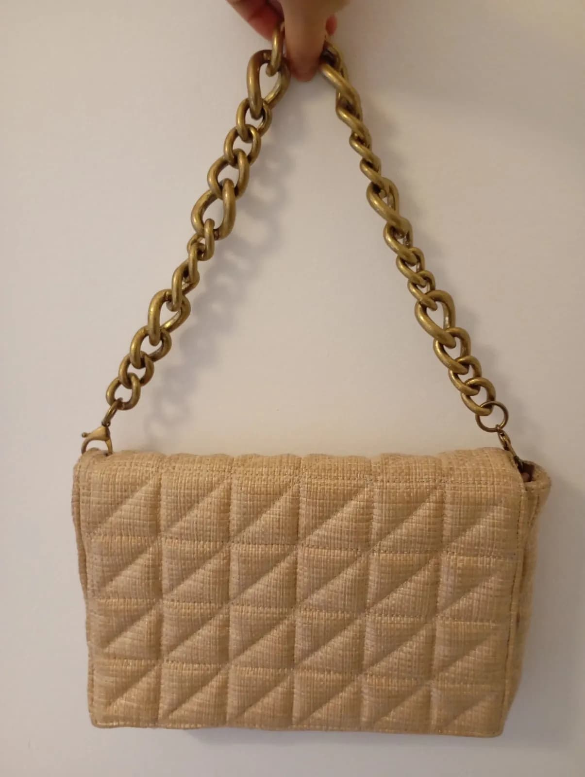 Bolso beige acolchado con textura de paja y cadena dorada.