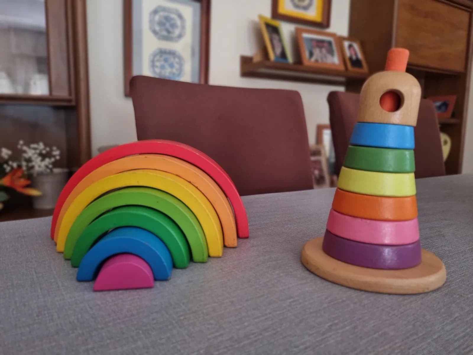 Dos juguetes de madera apilables de segunda mano: arcoíris y torre de anillos de colores.