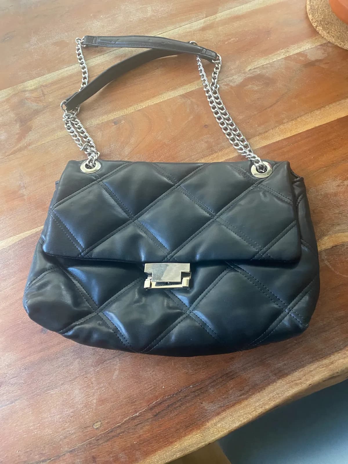 Bolso de solapa negro acolchado con correa de cadena y cierre plateado.