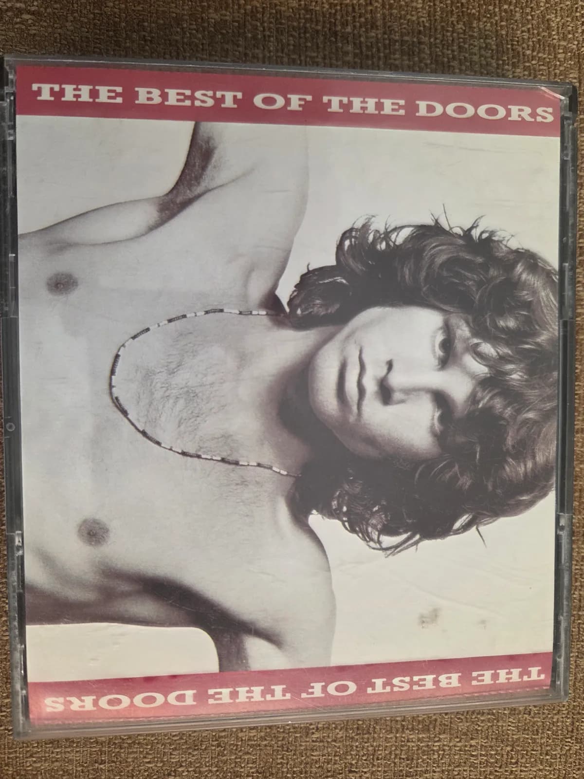 CD The Best of The Doors con Jim Morrison sin camiseta en portada, blanco y negro.